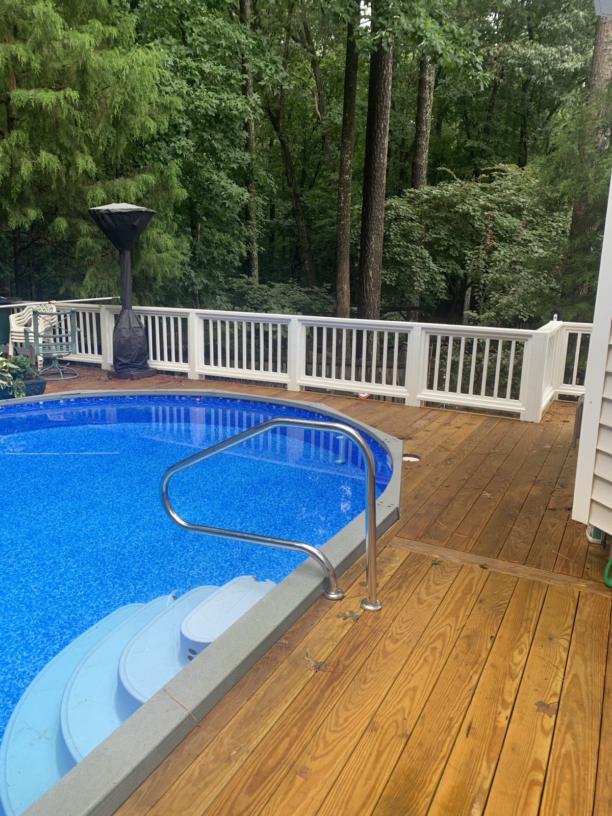 A wraparound pool deck with white railing and warm decking — safe footing and clean lines all the way around the water.